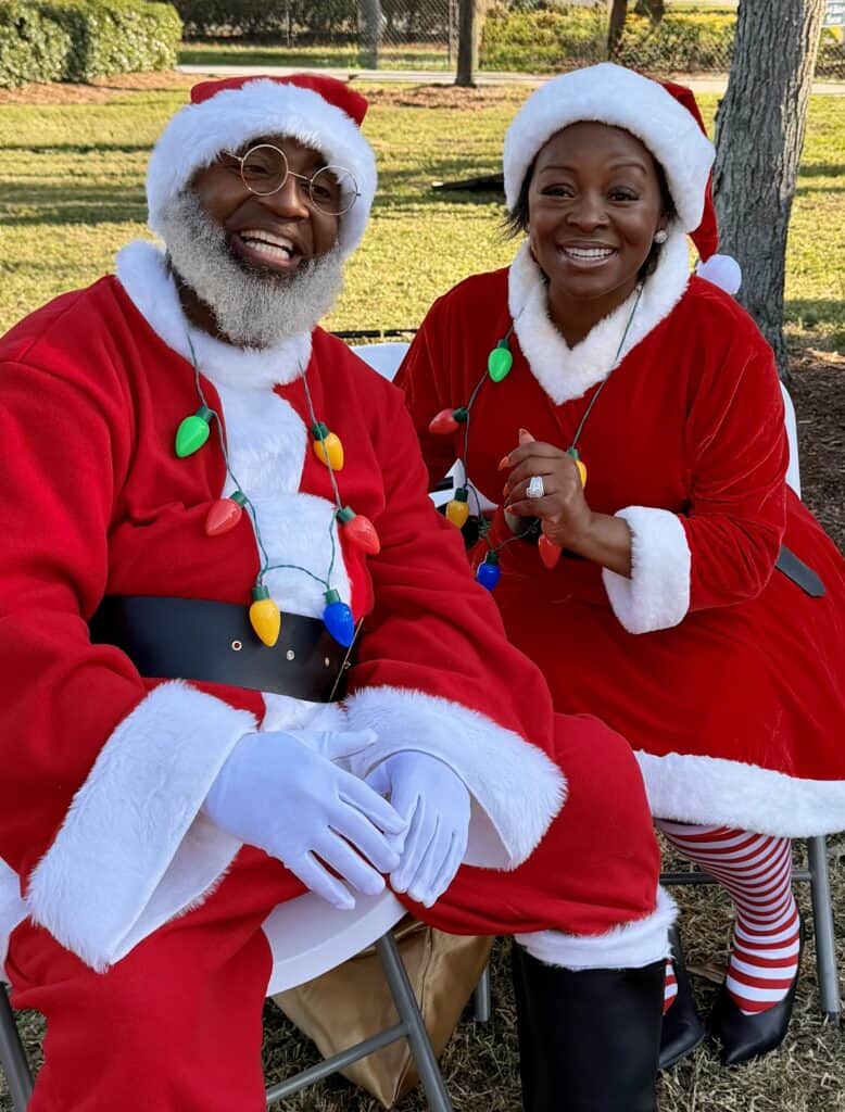 Santa and Mrs. Claus in holiday costumes smiling outdoors.
